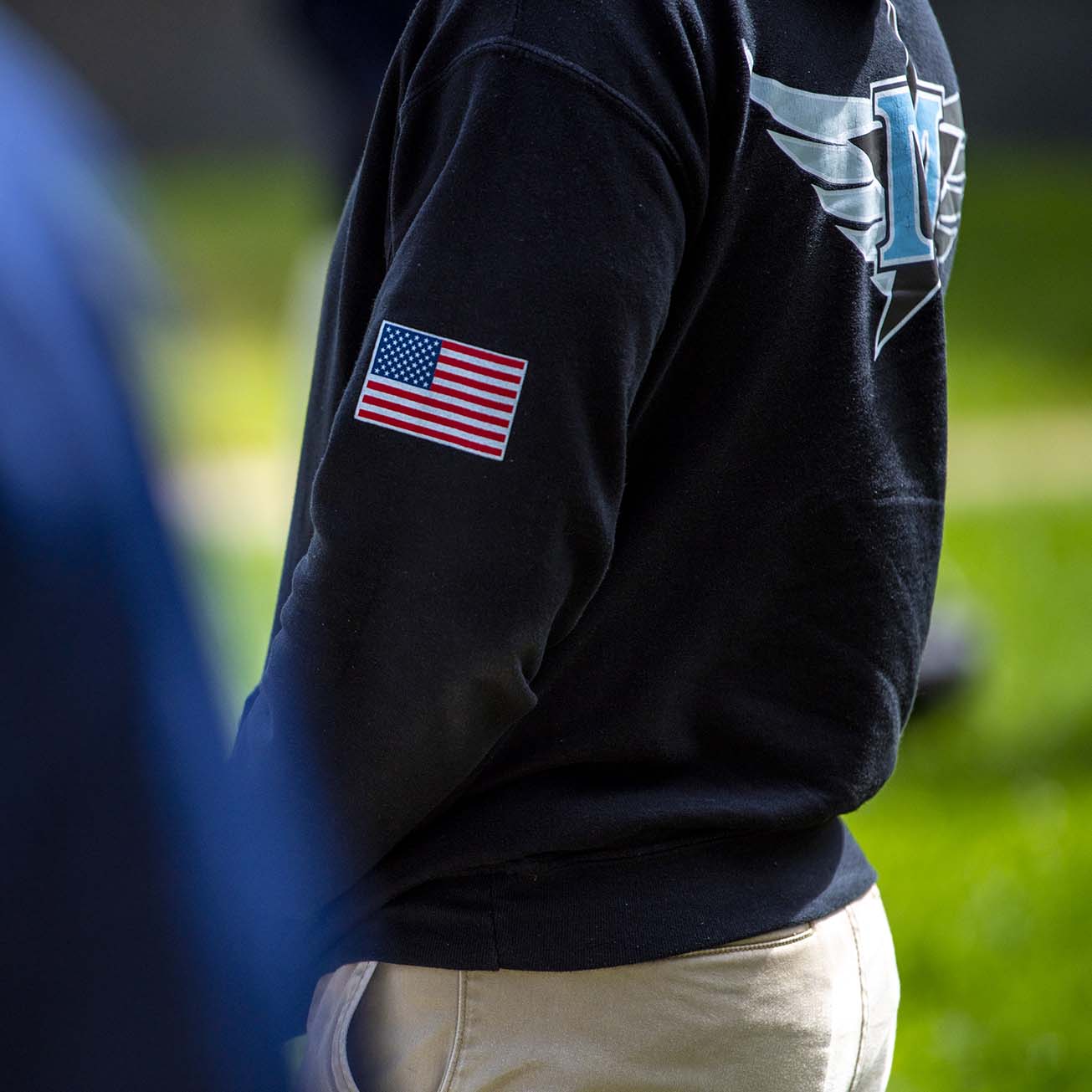 A photo of a person wearing a UMaine Veteran jacket with an American flag patch on the sleeve