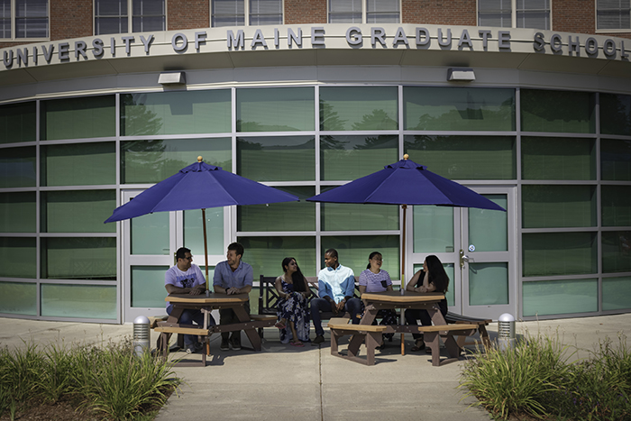 Students sitting at tables in front of the UMaine Graduate School