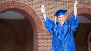 Mature adult in graduation cap and gown with hands up in celebration