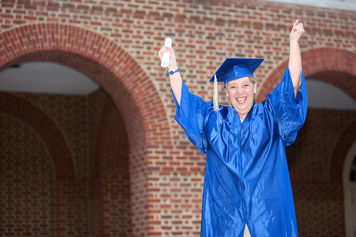 Mature adult in graduation cap and gown with hands up in celebration