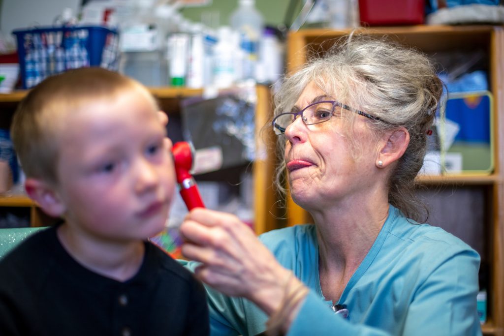 a photo of a older woman UMaine nursing student giving a young child an ear exam