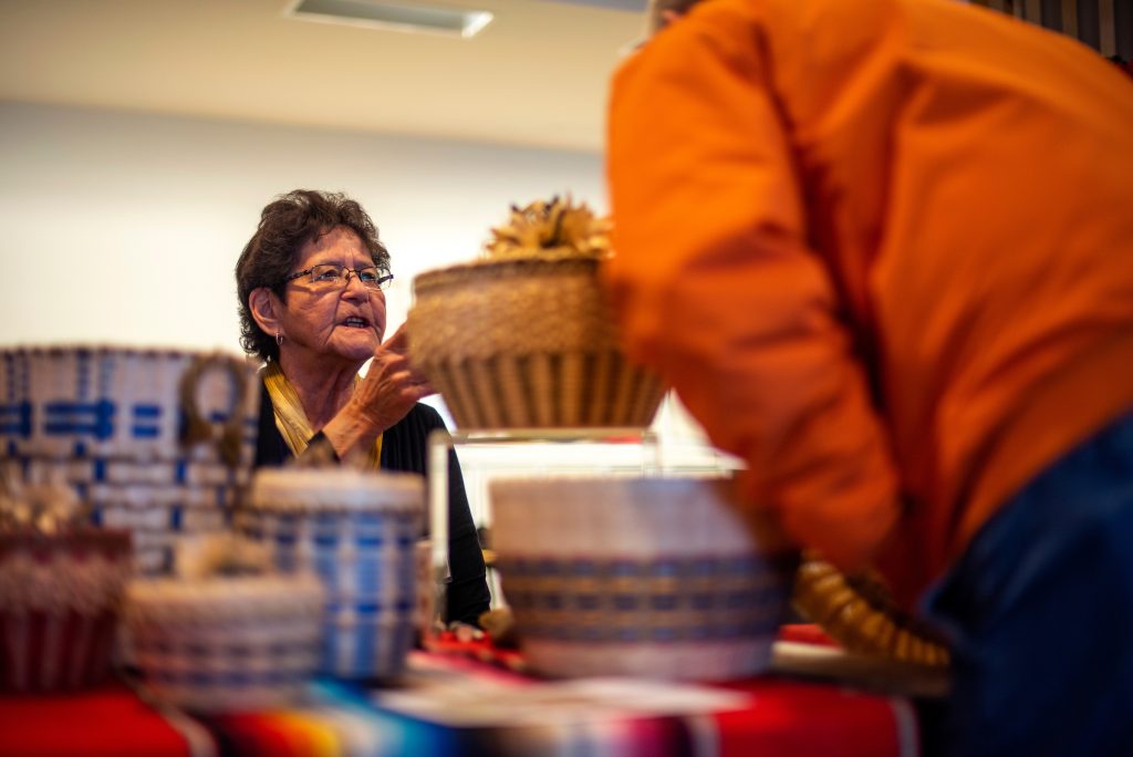 Older woman showing a handmade basked at the 2018 holiday basket market