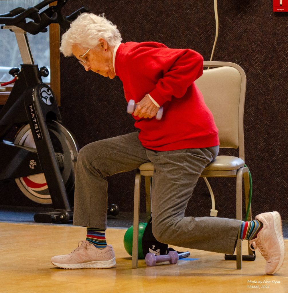 Older woman do a chair weight lifting exercise.