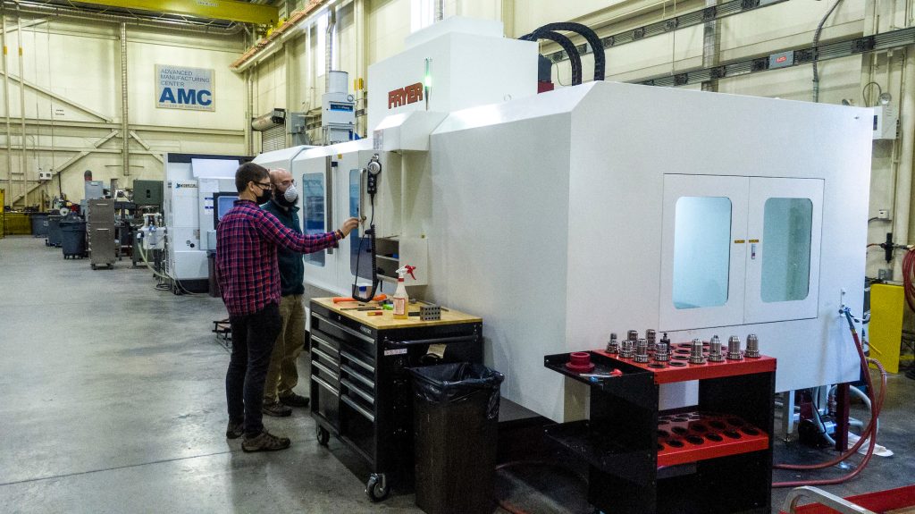 Project Manager Kyle Forsythe and student is Ezra Serdynski (red plaid shirt) use the AMC's new Fryer SX-100 5axis Machining center, testing some new tooling on a steel block to check material removal rate and surface finish.