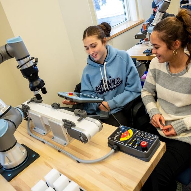 Two high-school students smiling while participating in universal robots co-bot workshop