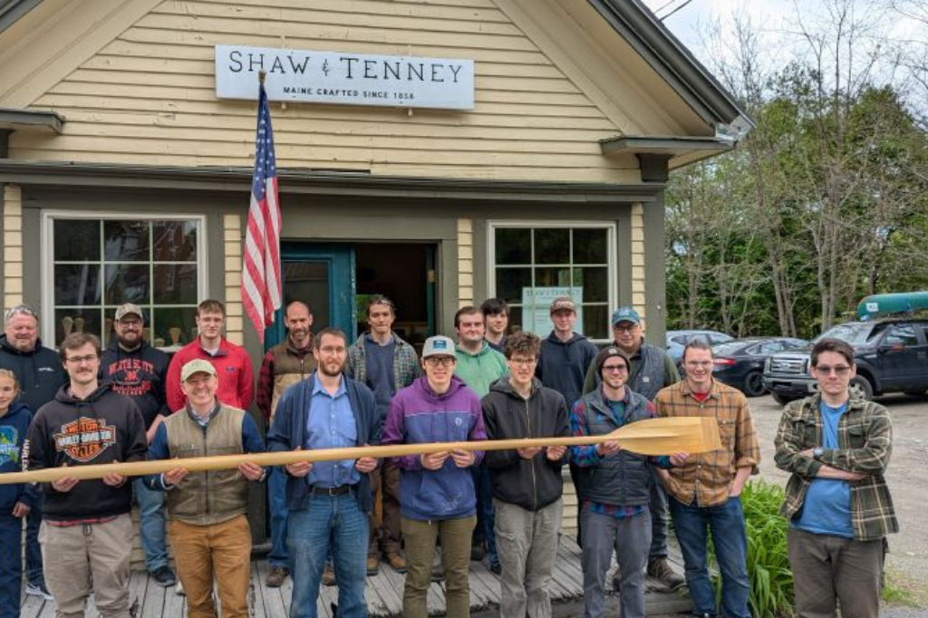 The Advanced Manufacturing Center team and student interns standing together holding a wooden oar at Old Town Canoe.