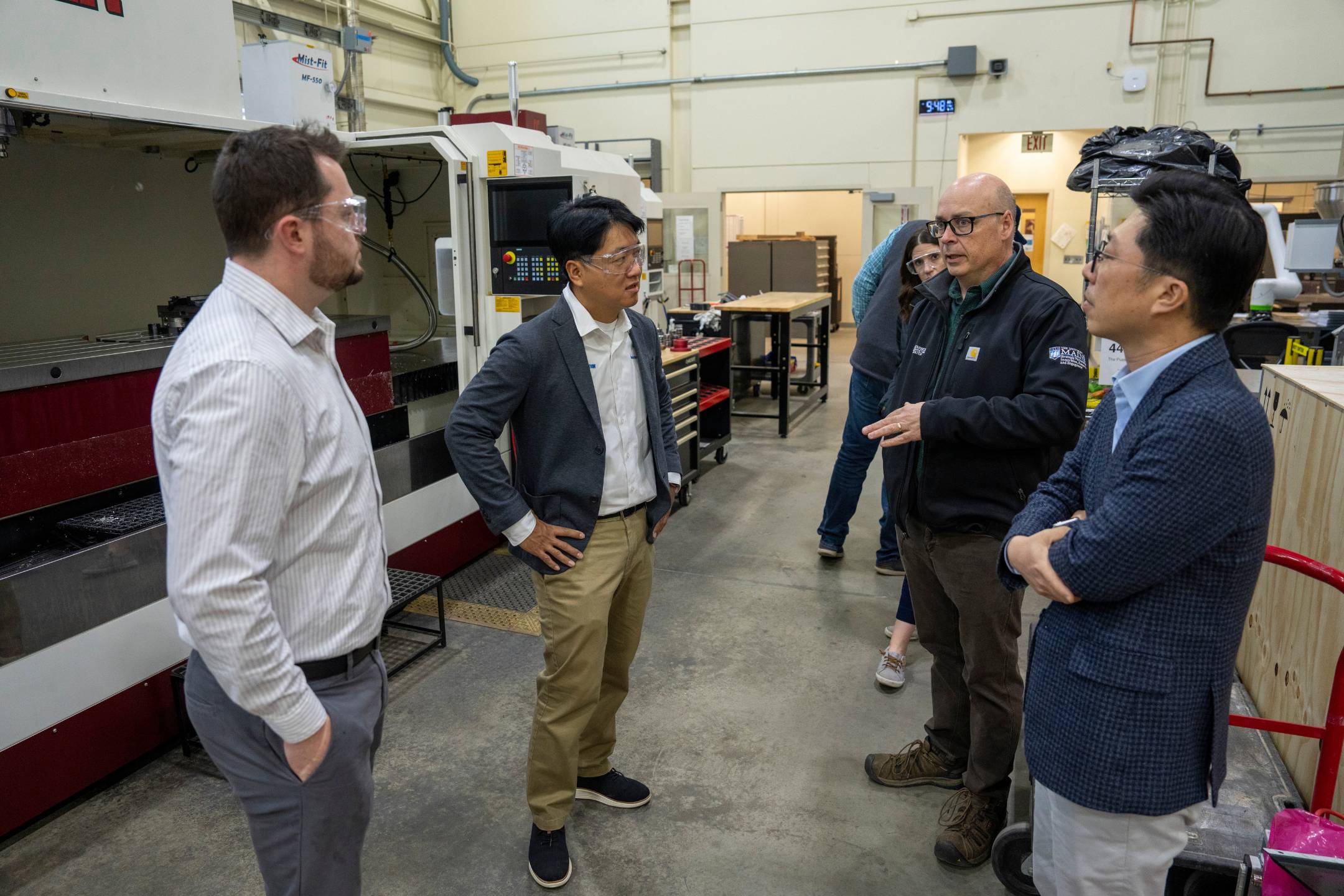 AMC leadership and visiting industry partners discuss equipment capabilities inside the Advanced Manufacturing Center's CNC lab during a facility tour.
