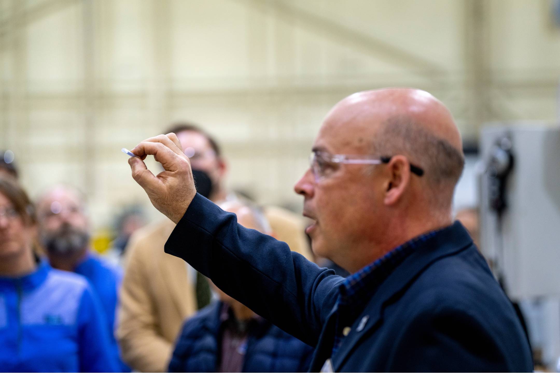 Director of the Advanced Manufacturing Center at the University of Maine holds up a machined part while speaking to visitors during a tour