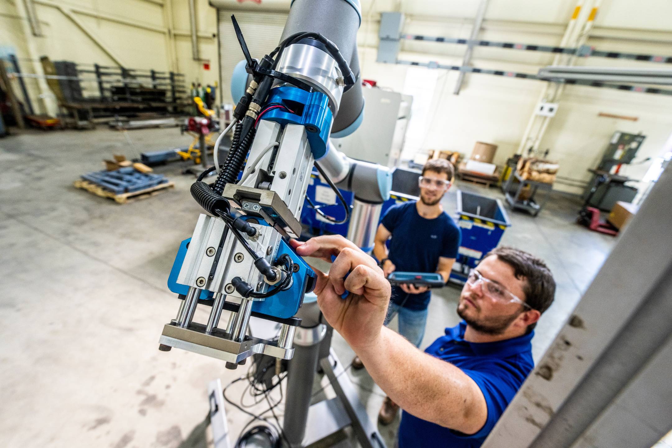 An Advanced Manufacturing Center staff member and a student at the University of Maine work together to adjust the gripper of a Universal Robots collaborative robot during technical training on the workshop floor.