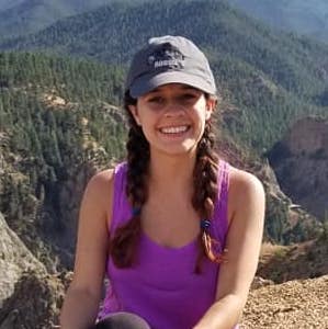 Photo of Christina McCosker sitting in front of valley filled with foliage. 