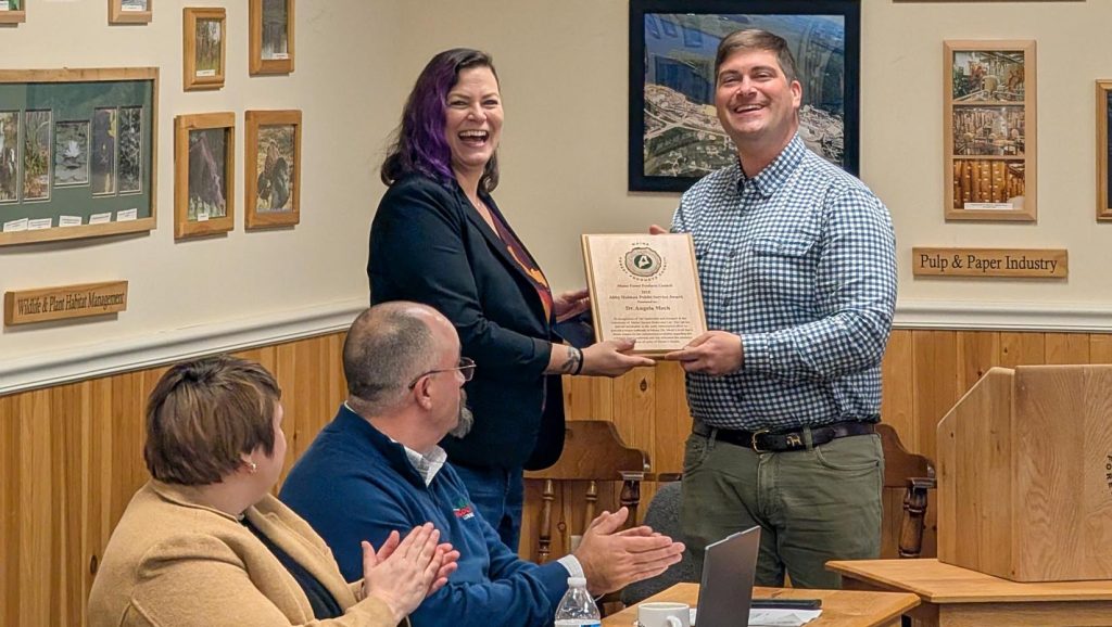 A photo of two people standing and holding an award in the background while two more people in the foreground clap.
