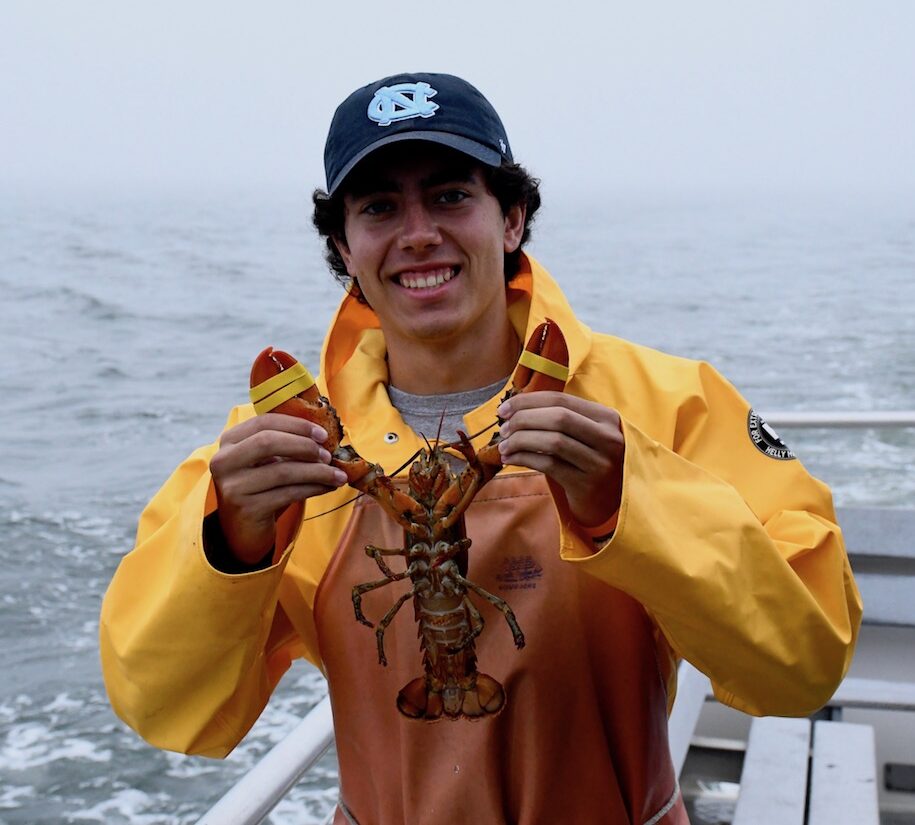 Kyle standing on a boat holding up a lobster