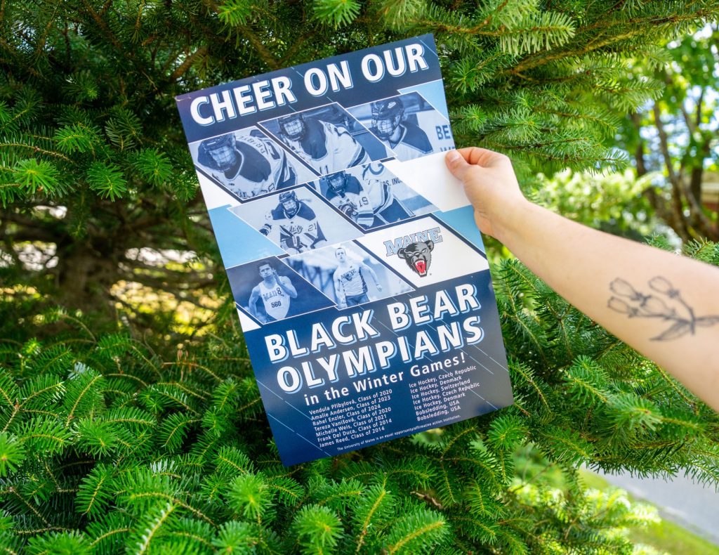 A photo of an arm holding a "Cheer On Our Black Bear Olympians" poster.