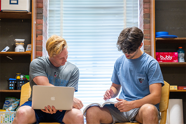 2 students in a dorm room looking at a computer