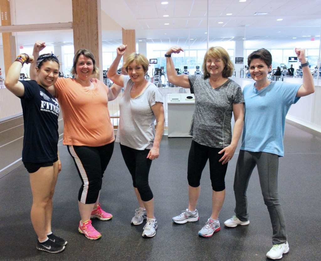 A fitness class poses for a photo, flexing their arms to show their strength