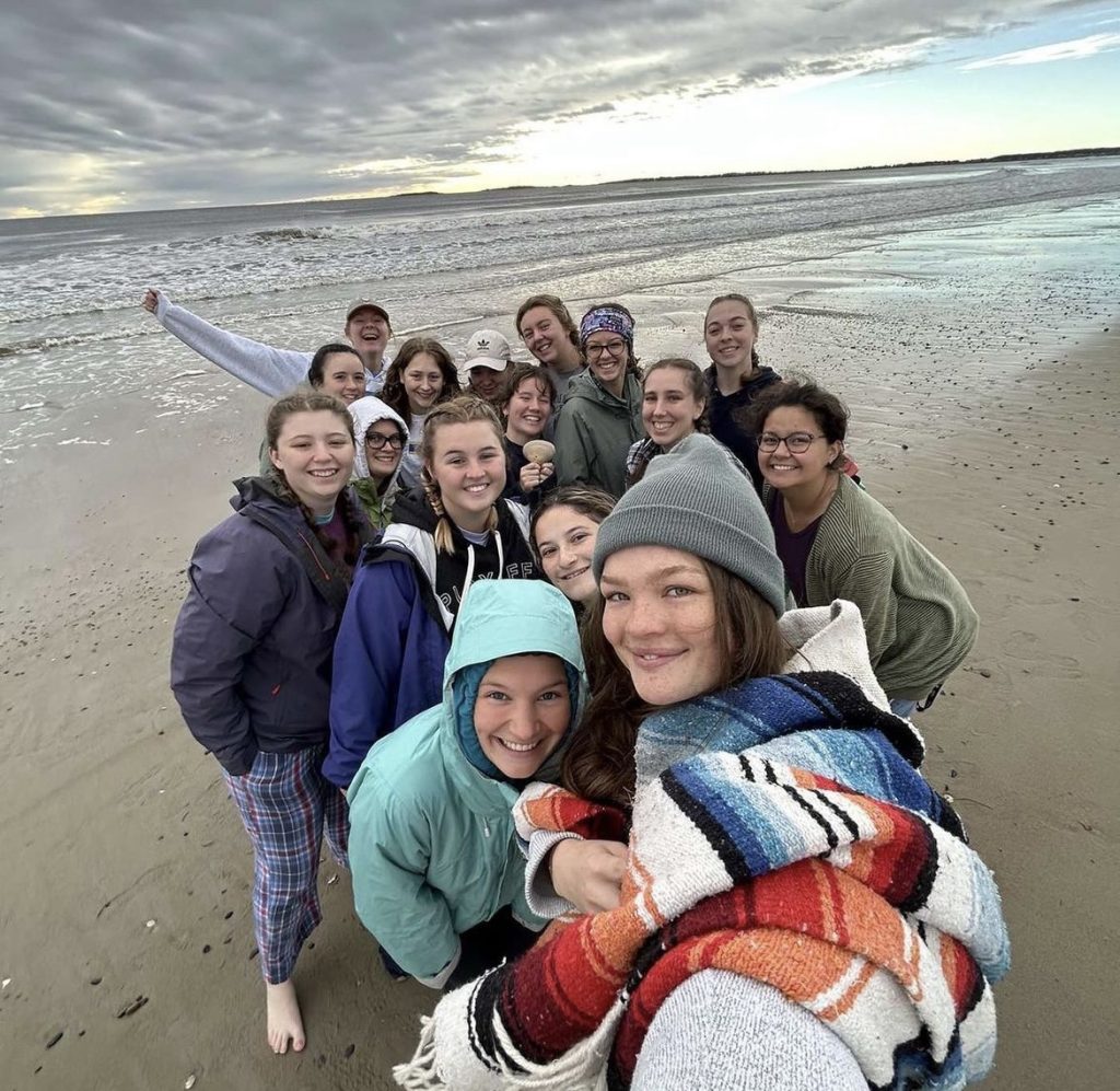 Women's Ultimate Frisbee club members gathering on the beach for a group photo.