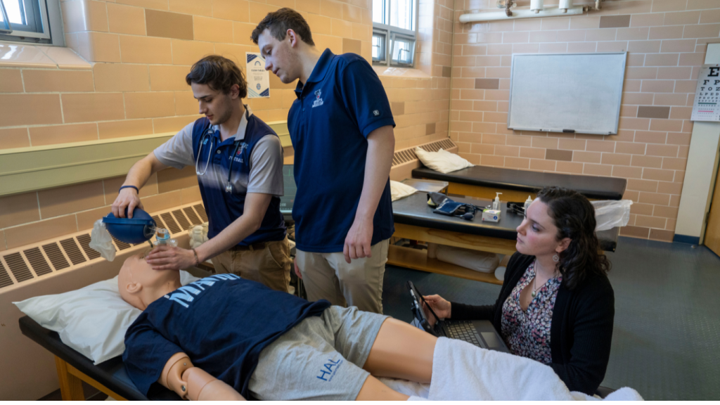 Two UMaine students practice administering first aid on Trauma HAL, an advanced trauma simulation dummy, while being observed by their professor, Dr. Shannon Wright. 