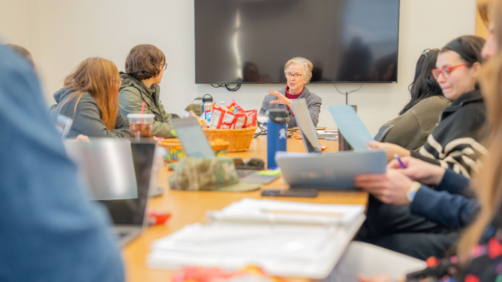 A group of student teachers looking toward the front of a meeting room, listening to a mentor teacher speak. 