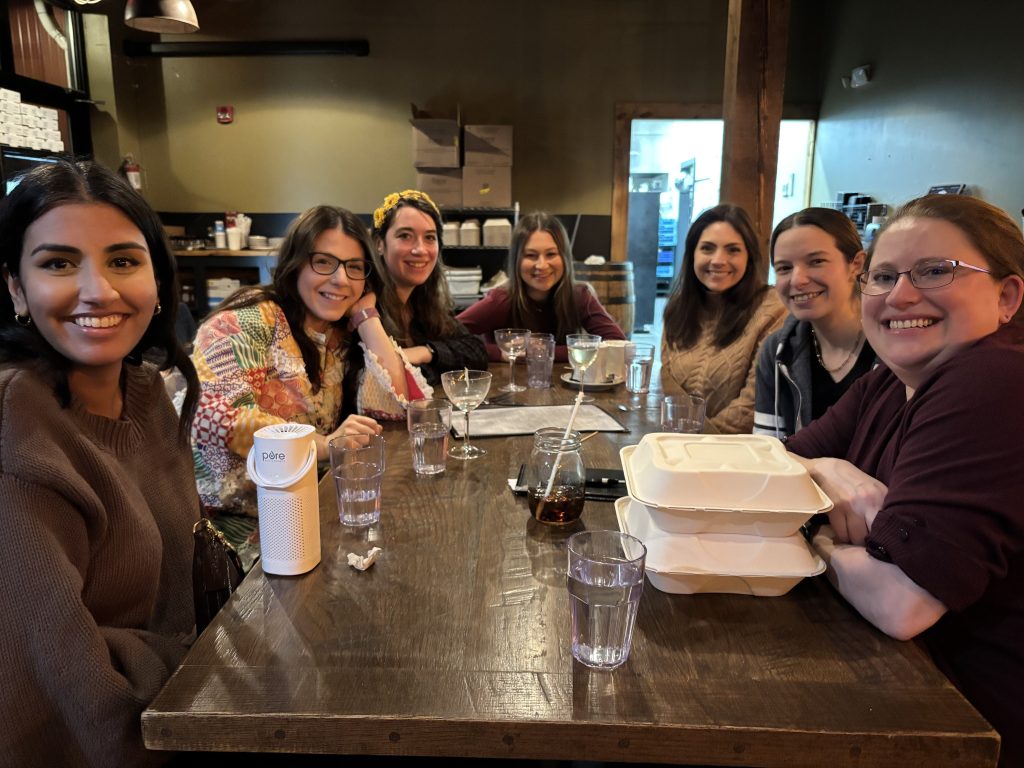 Puneet, Hannah, Aurora, Caroline, Katie, Eleanor, and Dr. Blossom smiling around a restaurant table