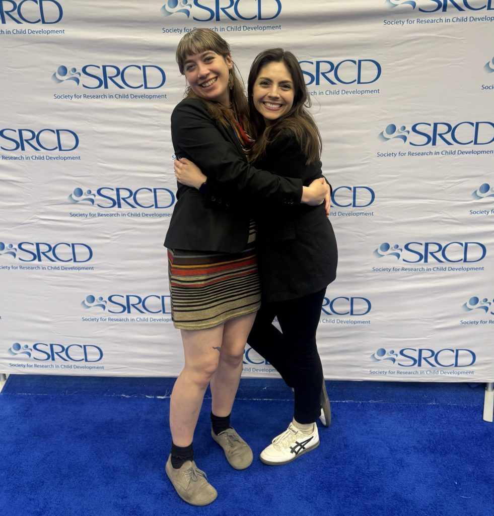 Aurora and Katie hugging in front of the SRCD background