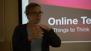 An instructor standing in front of a screen with the words Online Teaching in the background