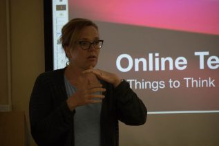 An instructor standing in front of a screen with the words Online Teaching in the background