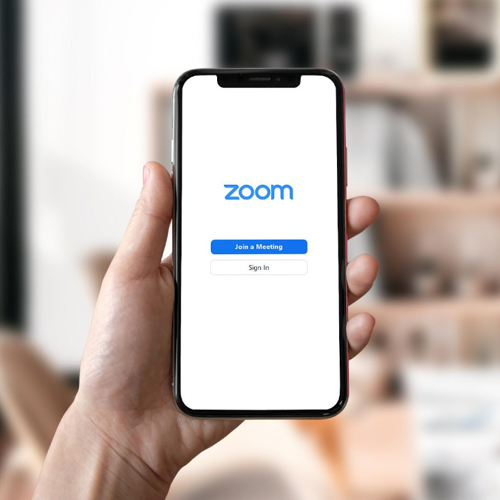 A hand holding a smartphone that displays Zoom's identification page.