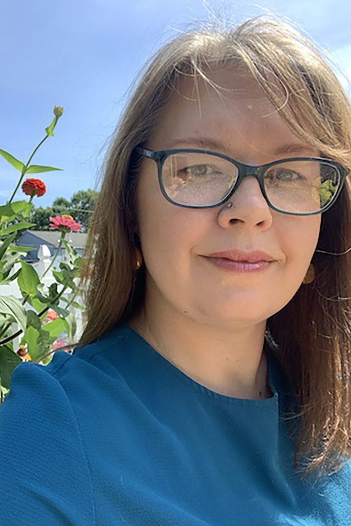 Photograph of Professor Falconer. Blue shirt with square glasses standing in front of flowers