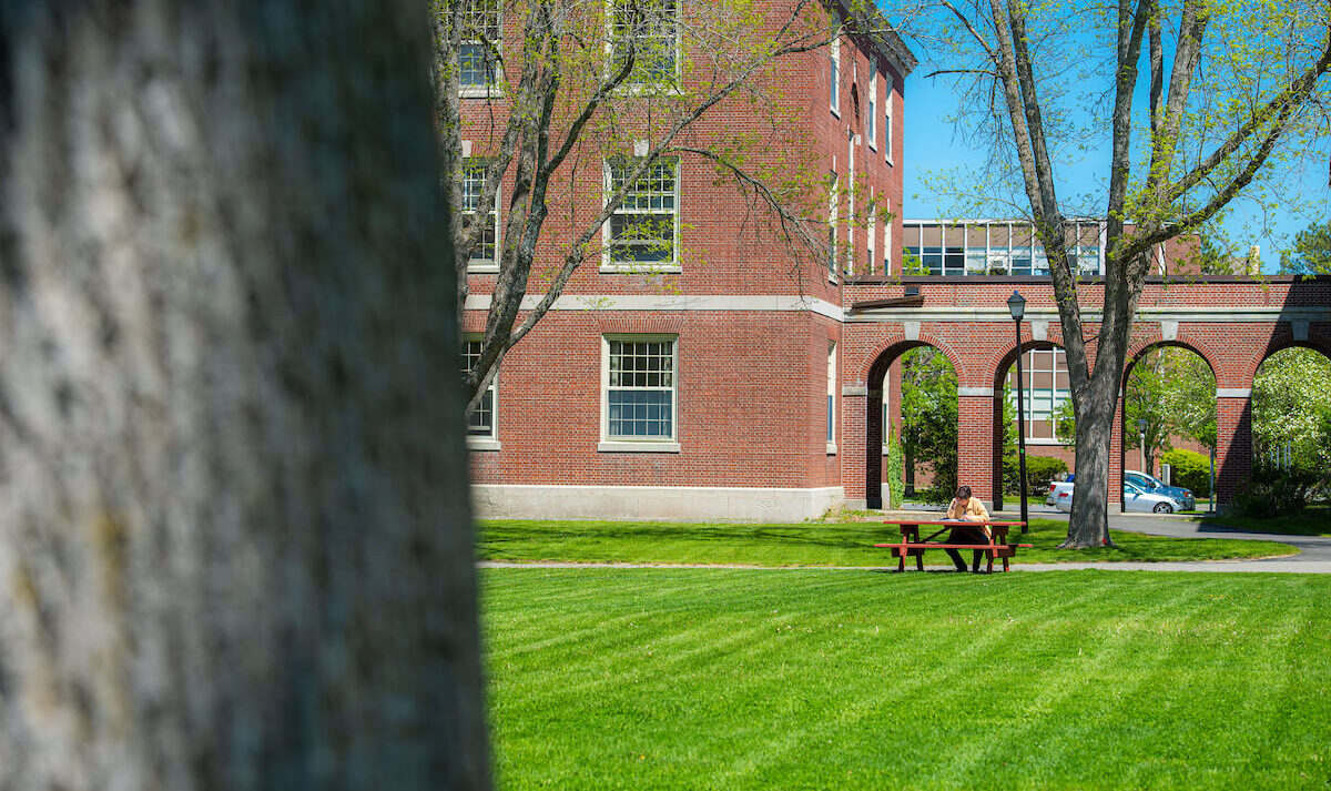 A student sits at a picnic table; Stevens Hall is in the background
