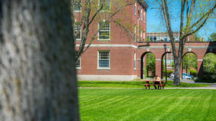 A student sits at a picnic table; Stevens Hall is in the background