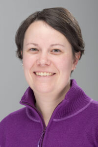 Portrait of Professor Leahy. She has short brown hair and is smiling at the camera. She wears a purple shirt with a zipper.