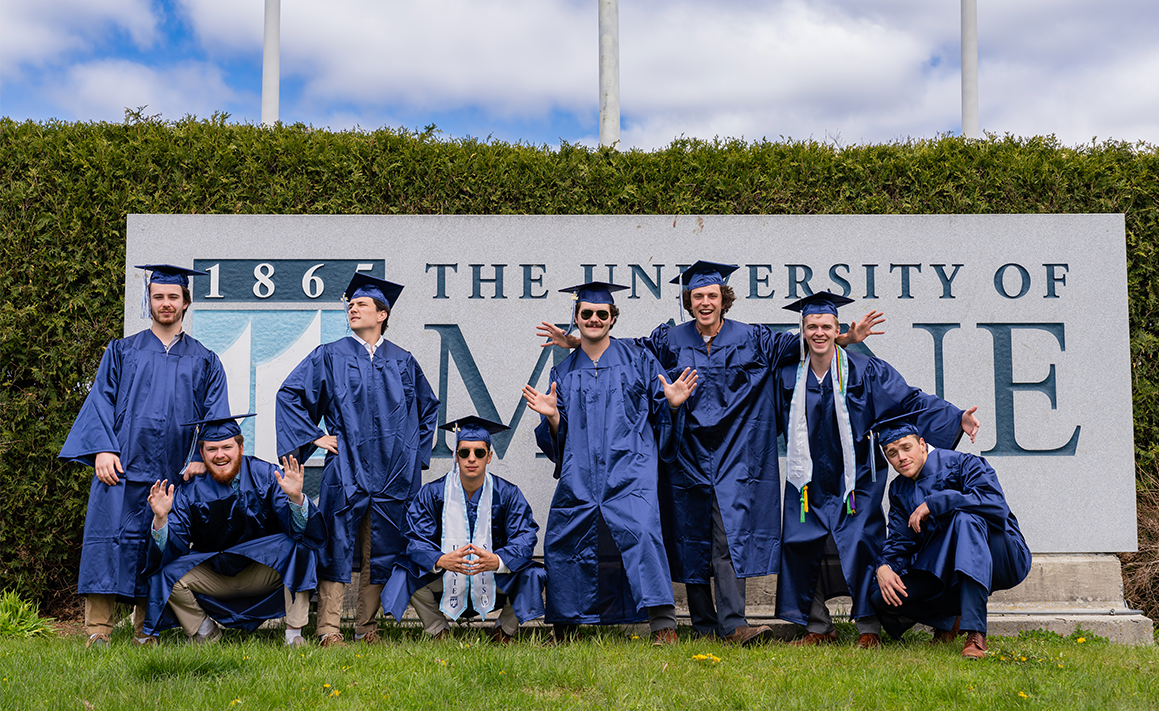 A photo of graduates by the University of Maine sign