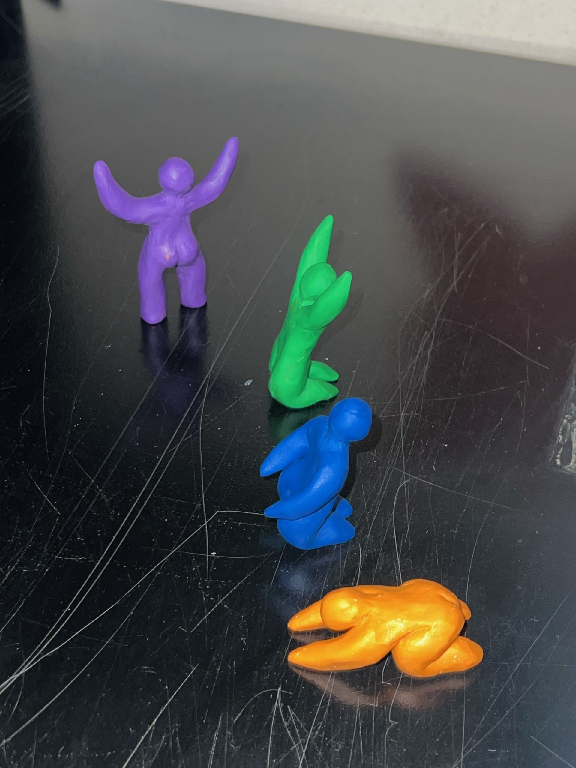 A photo of Elle Duncombe-Mills' humanoid figurines, 3D-printed in a variety of different solid colors, on a black tabletop.