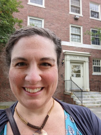 Meredith Eaton is smiling in front of Dunn Hall on the UMaine campus.