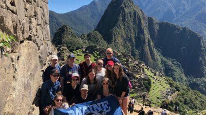 group of students on mountainside in Peru with UMaine banner