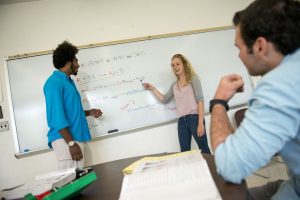 Students discussing work written on whiteboard