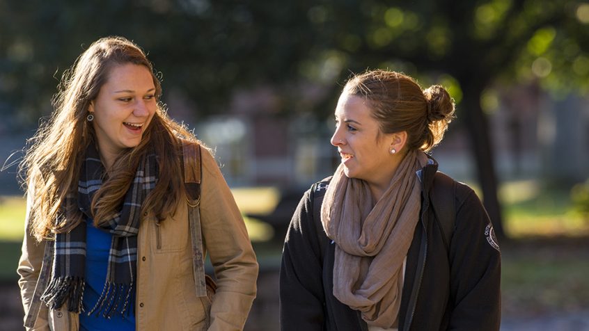 two student wearing jackets and scarves walking and talking outside.