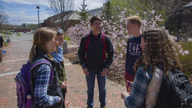 five students standing with backpacks on by flowering tree