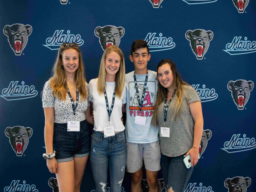Four students from Orientation standing in front of a UMaine banner