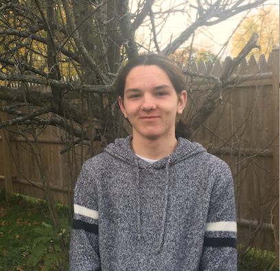 Male Student standing in front of a tree and fence