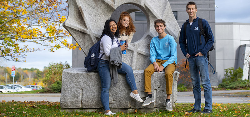 four students in front of sculpture on UMaine campus