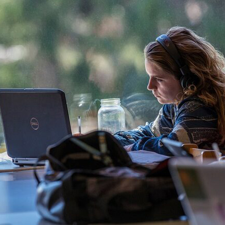 student watching labtop with headphones on and pen in hand
