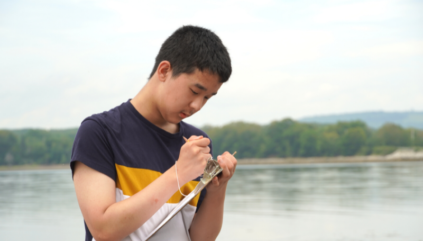 Student writes observations on clipboard, with ocean in the background.