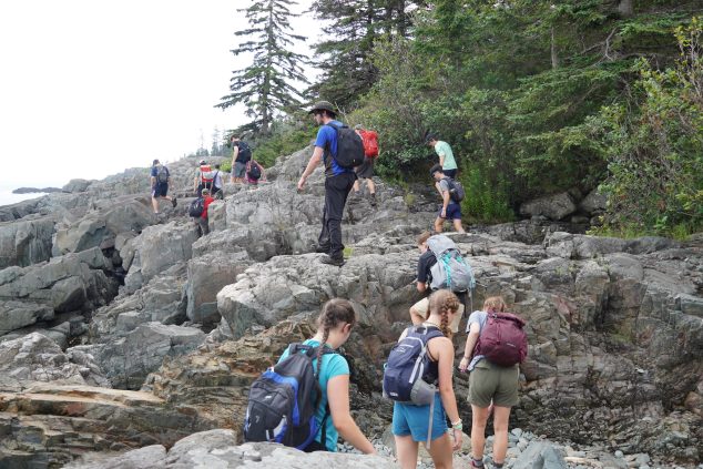 Students hike on rocky coastal boulders.