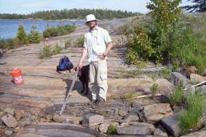 Jeff Marsh pointing to the layer containing an yttrium garnet, possibly a new mineral species, on Bonnet Island, Georgian Bay, Ontario. June 10, 2009