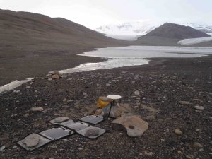 A solar-powered differential GPS is set up on a survey benchmark near the east end of Lake Miers in January 2011. The I-196 (Hall) camp is in the background near the south shore of the lake. Adams glacier is on the left at the far end of the lake, and Miers glacier is on the right. Ross Sea ice grounded in the mouth of the valley dammed a much larger lake during glacial times. GPS elevations on deposits formed near the shore of this paleo-lake define a minimum thickness for the former Ross Sea Ice Sheet.