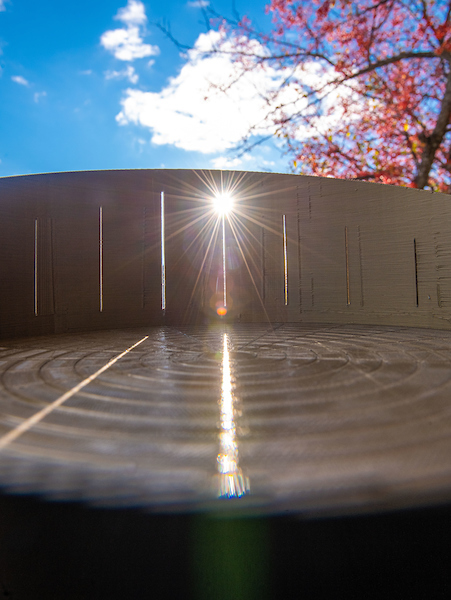 A prototype that uses rays of sunlight to conduct multiplication and division operations rests beneath a sunny sky near the UMaine sculpture studio
