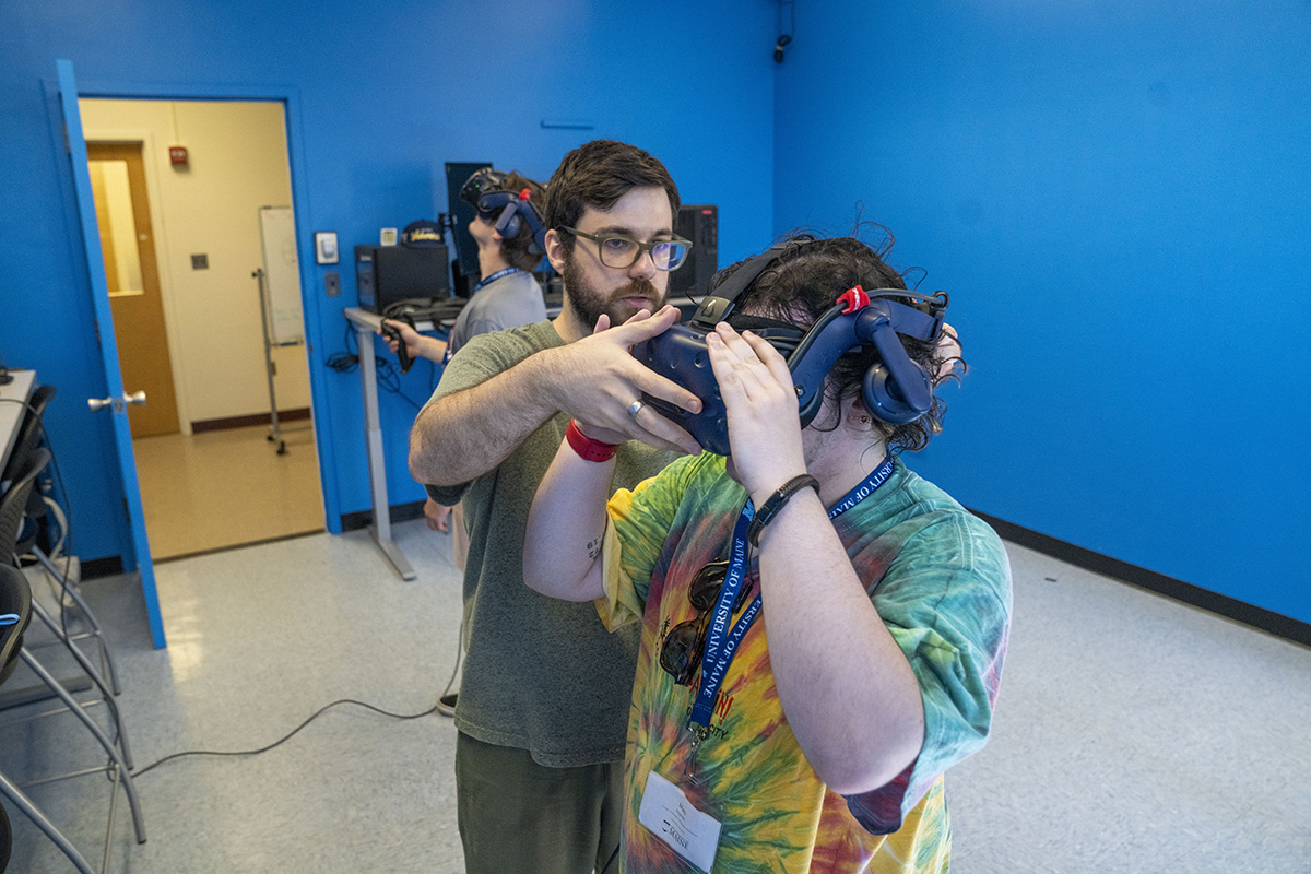 Izge Bayyurt, a Master of Science in Teaching student and graduate research assistant with the University of Maine College of Education and Human Development's Immersive Mathematics in Rendered Environments Lab, assists an incoming freshman student with a virtual reality headset during UMaine's New Student Orientation on June 20, 2024. Photo courtesy University of Maine.