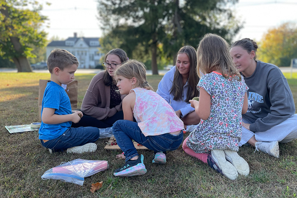 Education students sitting in grass with children