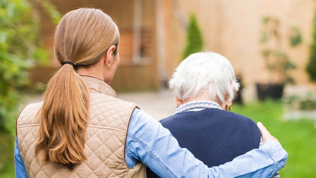 A photo of two people walking outside. The person on the left has their arm wrapped around the person on the right.